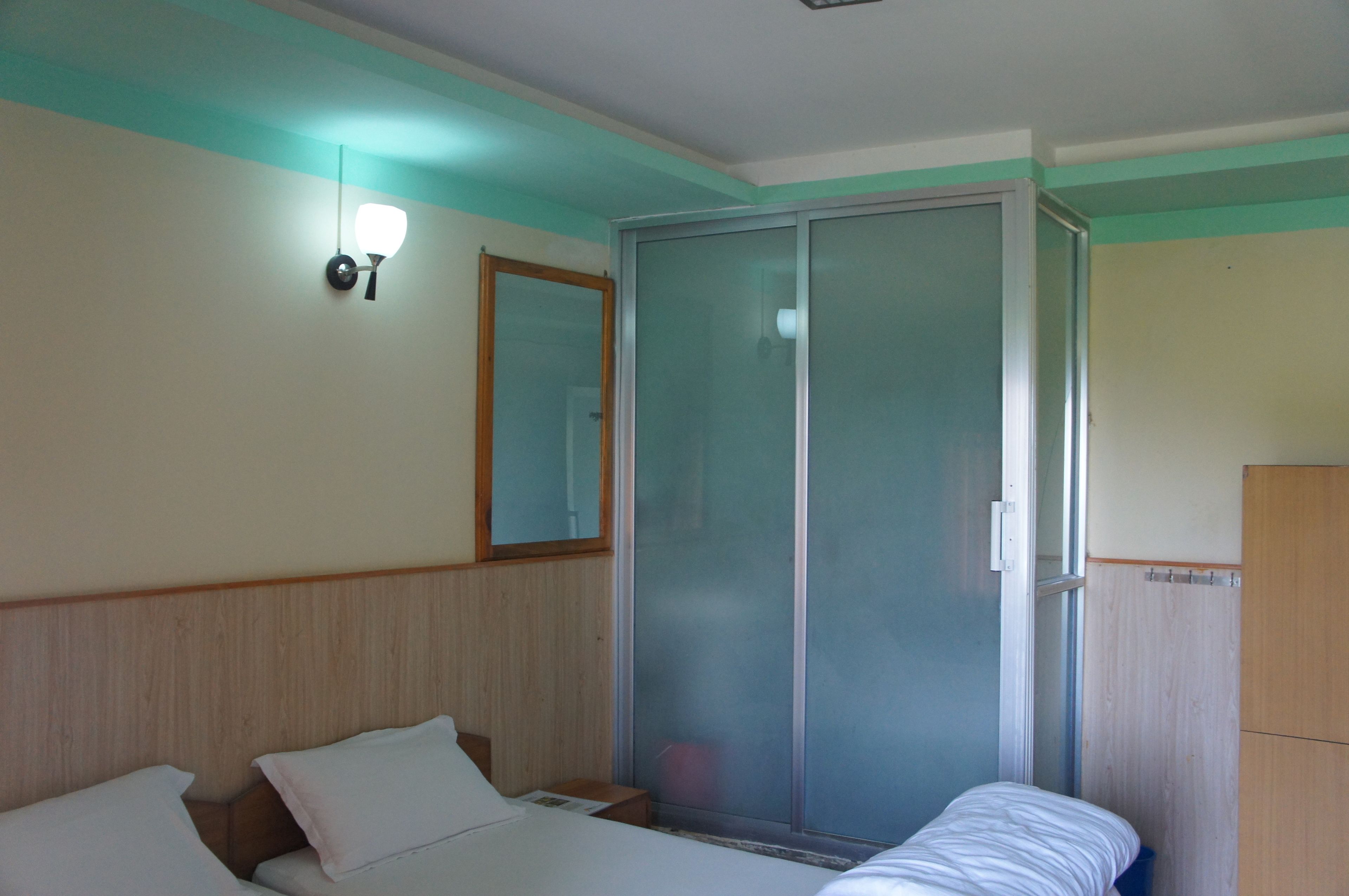 A hotel room with a bed, a wardrobe, a mirror, and a wall-mounted light fixture.