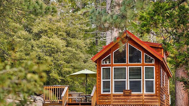 A wooden cabin with a large window, a deck with a table and chairs, and a sign that reads "Sugar Pine."