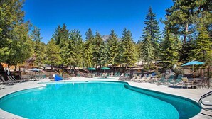 A pool with a 'NO JUMPING' sign, surrounded by lounge chairs and umbrellas, with trees in the background.