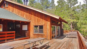 A wooden cabin with a deck, picnic tables, and a covered outdoor seating area.