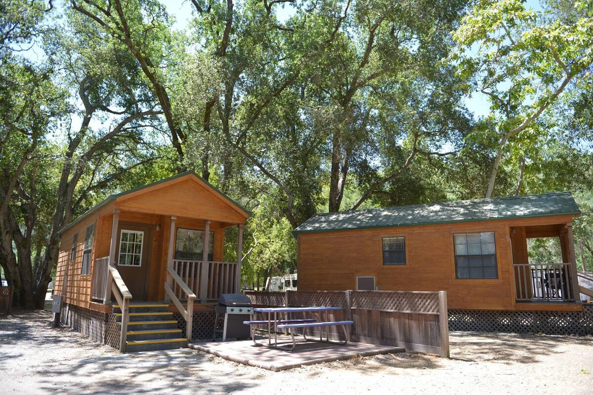 A wooden cabin with a porch, a barbecue grill, and a picnic table.