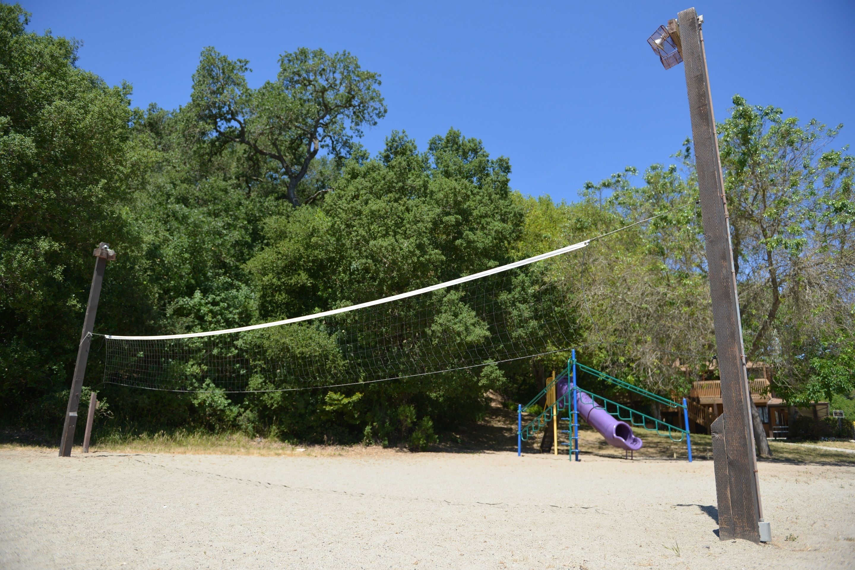 A playground with a netted volleyball court, a slide, and a swing set.