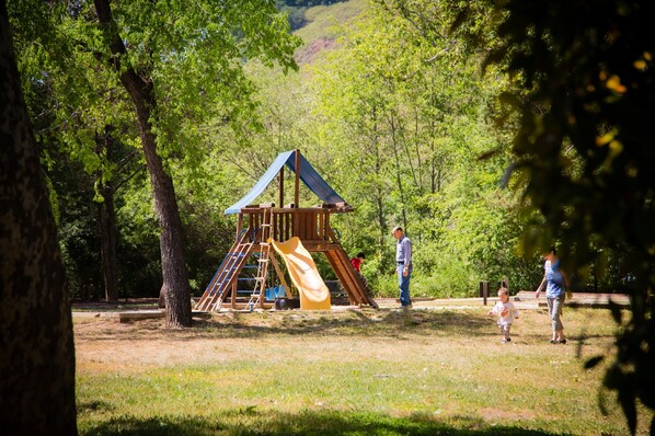 Un parque infantil con tobogán y estructuras para escalar, rodeado de árboles.