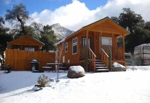 A wooden cabin with a porch, a staircase, and a snow-covered ground. - Oakzanita Springs RV Campground (Descanso)