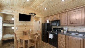 A wooden cabin interior with a dining area, kitchen, and a sleeping loft. - Palm Springs RV Resort (Palm Desert)
