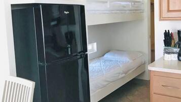 A compact room with a black refrigerator, a bunk bed, a small kitchen area, and a wooden cabinet.