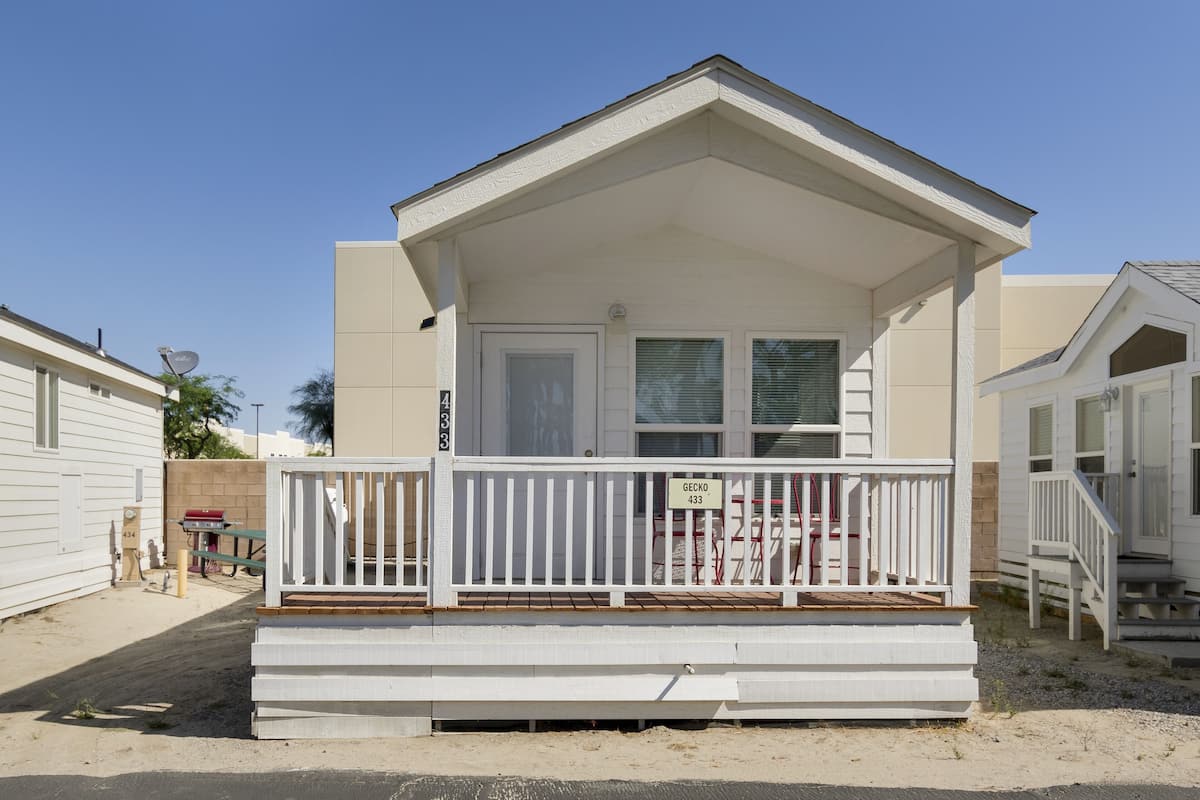 A single-story mobile home with a white exterior, a front porch with a white railing, and a sign that reads "GECKO 433".