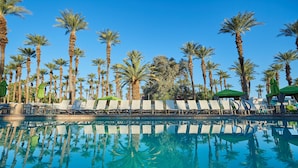 A poolside area with lounge chairs and umbrellas, surrounded by tall palm trees. - Palm Springs RV Resort (Palm Desert)