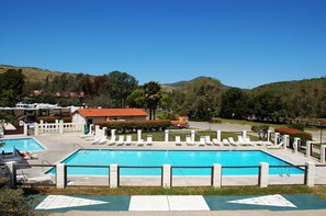 A swimming pool with lounge chairs and a fenced area, surrounded by hills and trees.