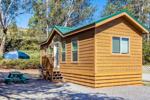 A wooden cabin with a green roof, a picnic table, and a covered umbrella.