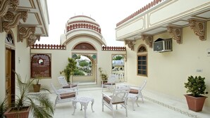 An outdoor seating area with white chairs and tables, surrounded by ornate architectural details and potted plants. - Madhuban - A Heritage Home (Jaipur)