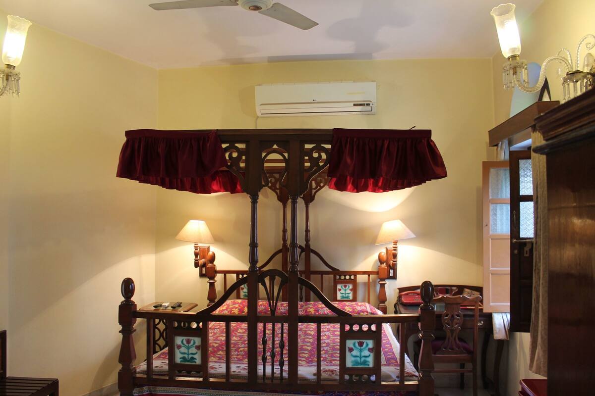 Un dormitorio con una cama con dosel, dos lámparas fijadas a la pared, un aire acondicionado y un ventilador de techo.