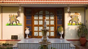 A building entrance with a wooden door, two wall murals of elephants, a fountain, and potted plants. - Madhuban - A Heritage Home (Jaipur)