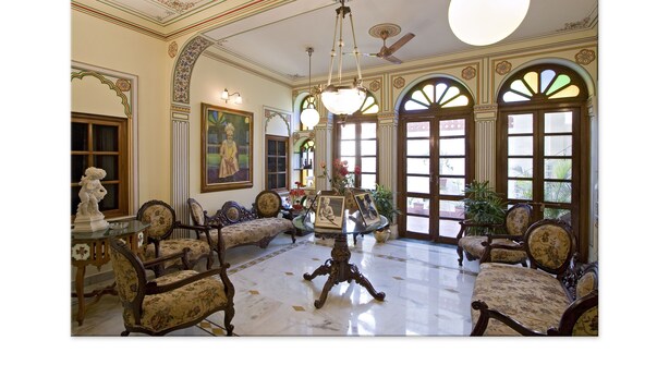 A spacious room with ornate furniture, large windows, and a ceiling fan. - Madhuban - A Heritage Home (Jaipur)