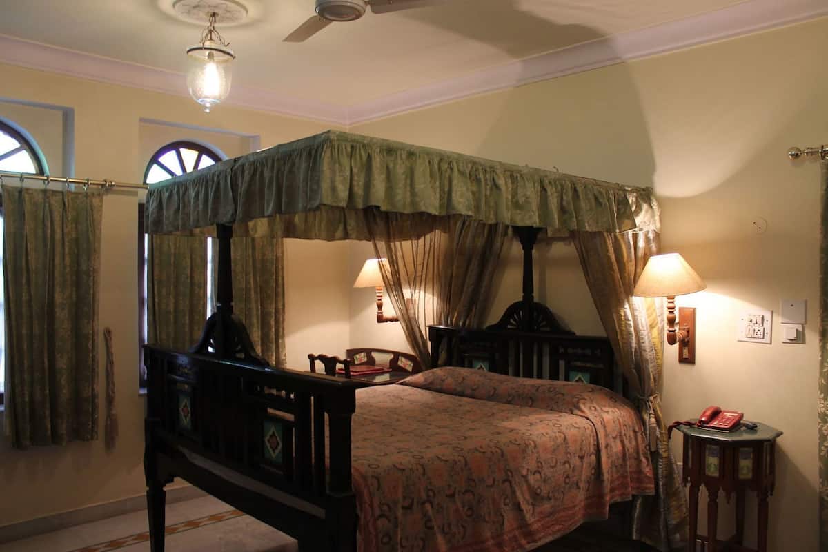 Una cama con dosel, dos lámparas de noche, una mesita de madera y una silla.