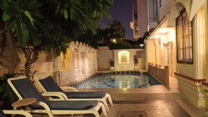 A swimming pool with lounge chairs and a decorative wall. - Madhuban - A Heritage Home (Jaipur)