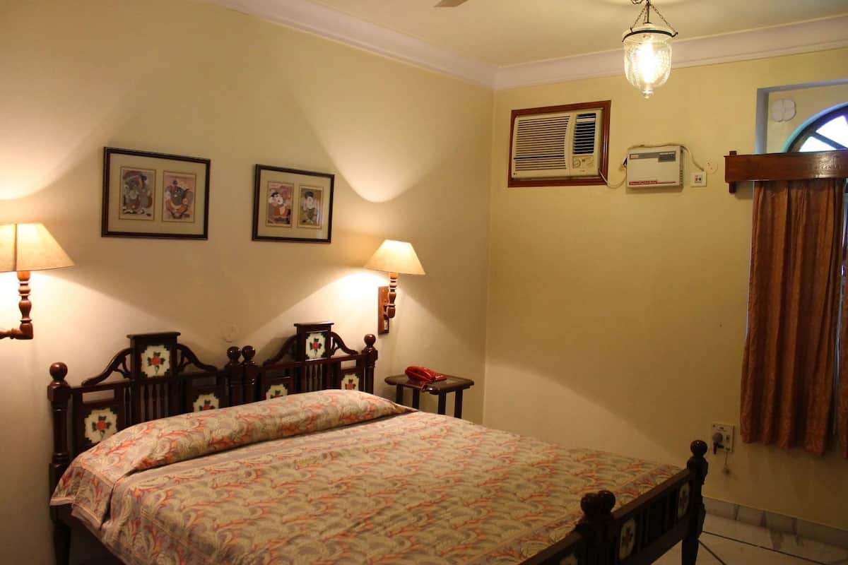 Un dormitorio con una cama doble, dos lámparas de pared, un equipo de aire acondicionado y una ventana con cortinas.