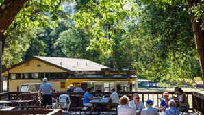 An outdoor dining area with wooden tables and benches, surrounded by trees. - Russian River RV Campground (Cloverdale)