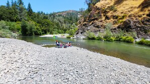 A riverbank with a rocky shore and a group of people sitting by the water. - Russian River RV Campground (Cloverdale)