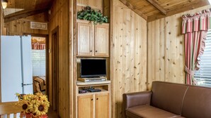 A wooden interior with a brown leather sofa, wooden cabinets, a television, and a vase of sunflowers. - Russian River RV Campground (Cloverdale)