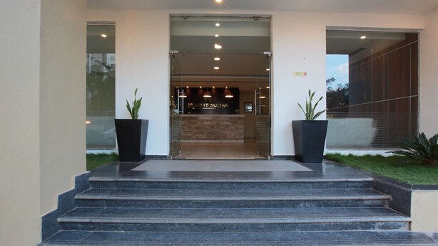 A modern building entrance with a reception desk, glass doors, and a staircase leading up. - Starlit Suites bangalore (Anekal)