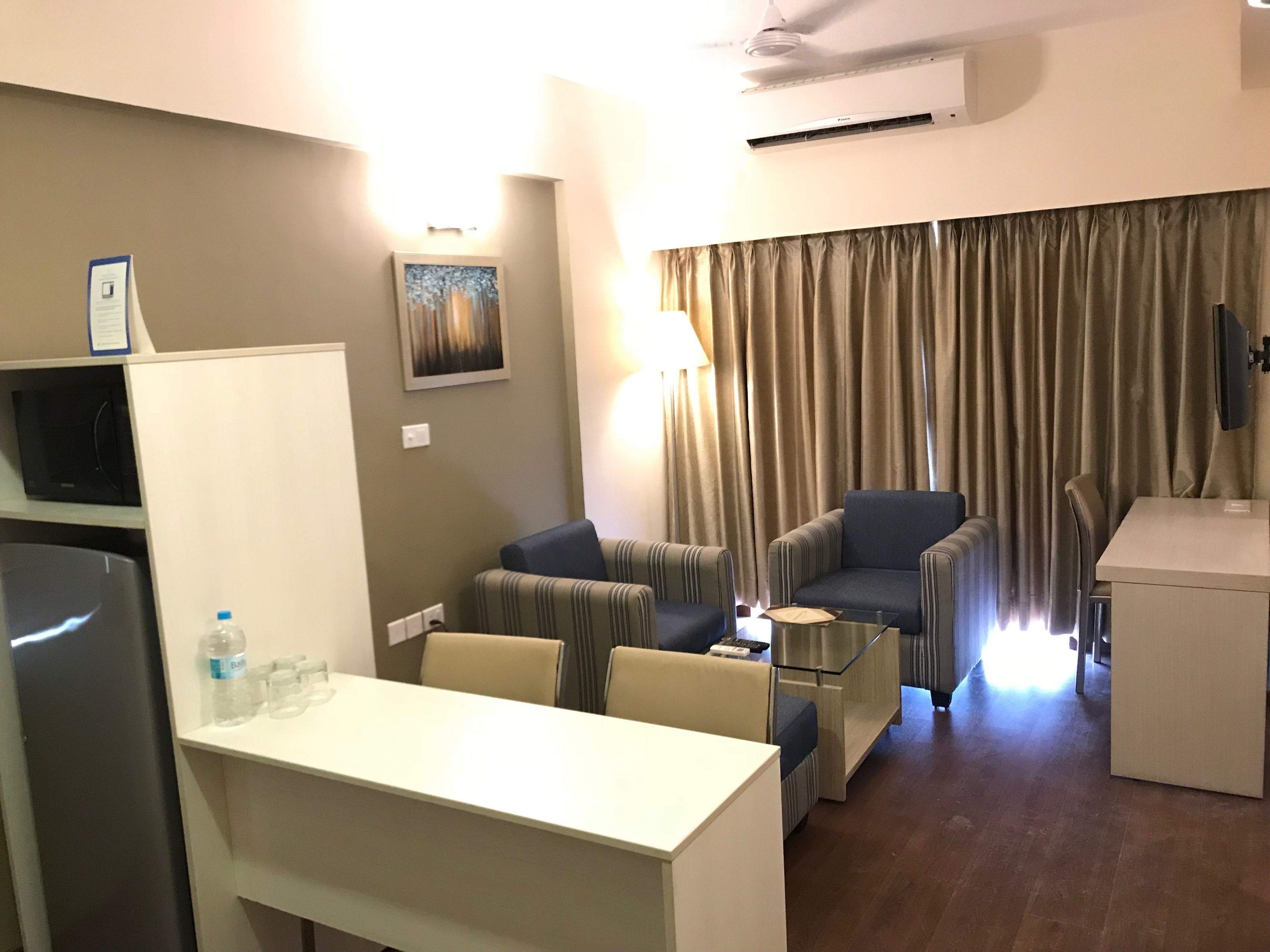 A hotel room with a dining area, a sofa set, a TV, and an air conditioning unit.