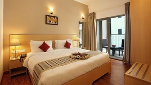 A hotel room with a large bed, bedside lamps, a telephone, a painting on the wall, and a balcony with chairs. - Starlit Suites bangalore (Anekal)