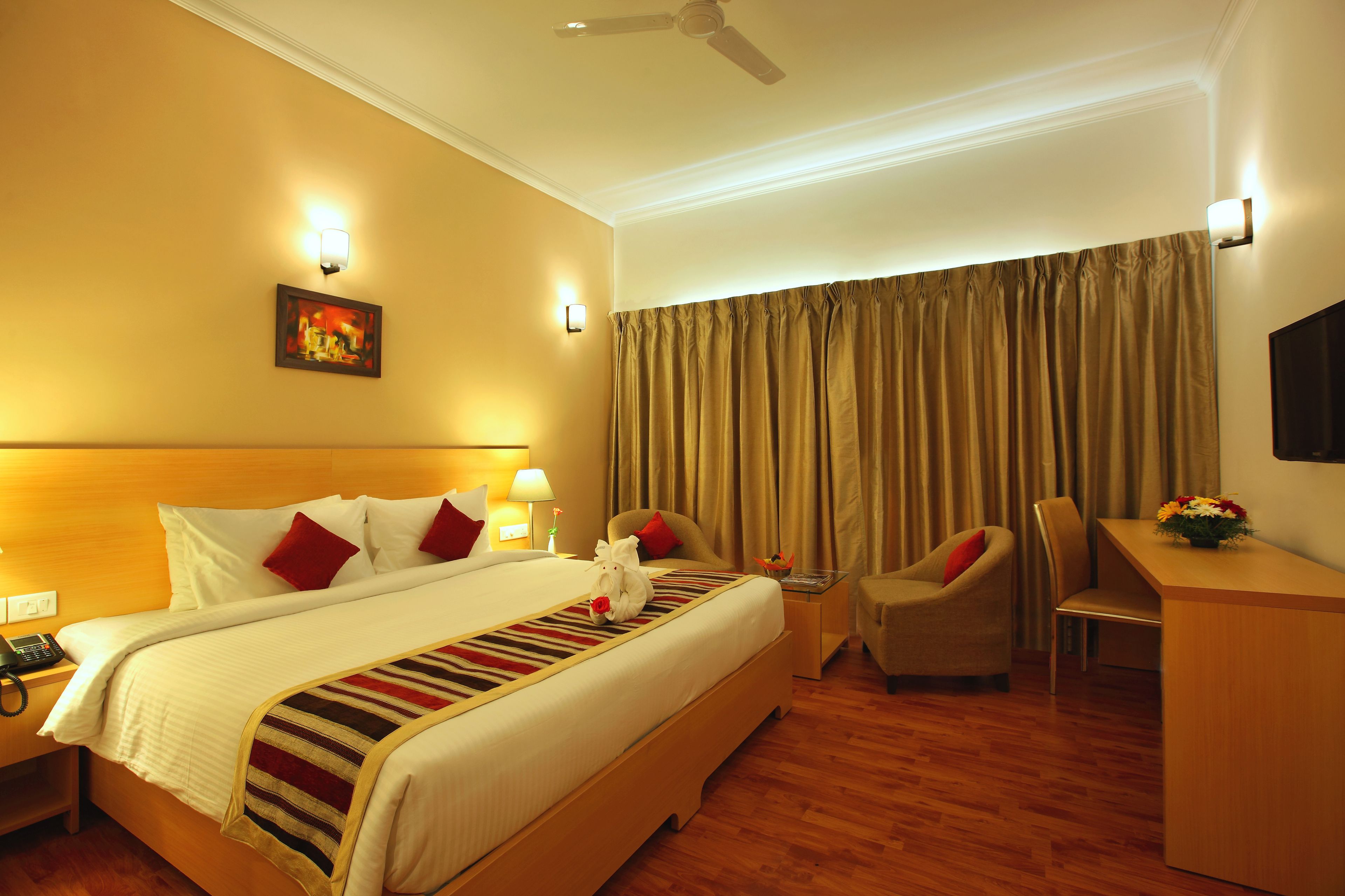 A hotel room with a large bed, a desk, a chair, and a ceiling fan.