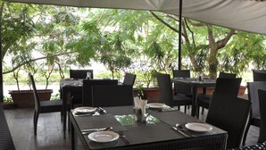 An outdoor dining area with tables and chairs, surrounded by potted plants and trees. - Starlit Suites bangalore (Anekal)