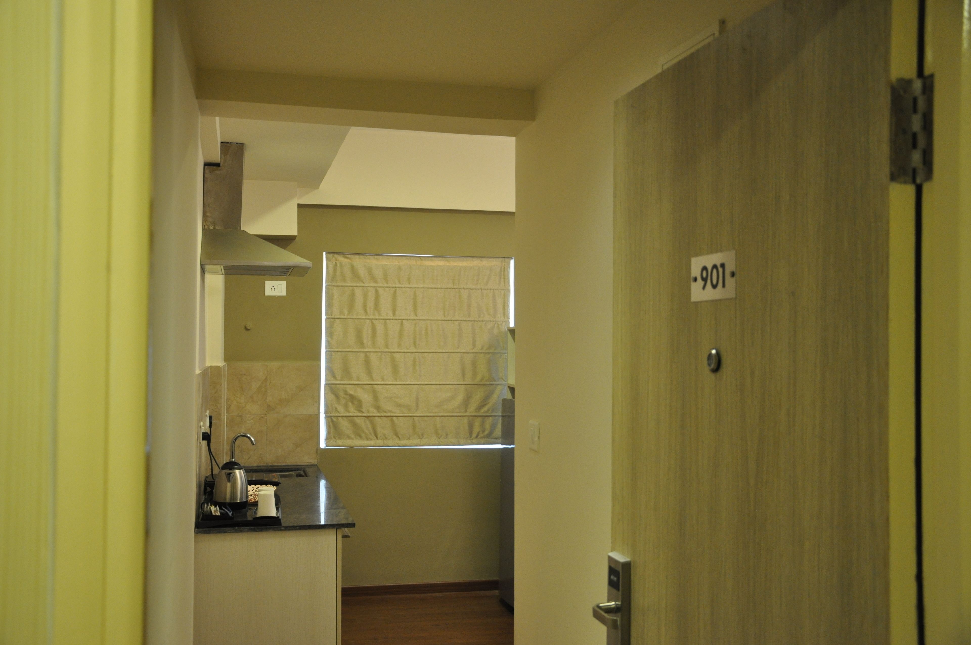 Ein schmaler Flur führt zu einem Zimmer mit Fenster, einer Tür mit der Nummer 901 und einer Küchenzeile mit Wasserkocher und Toaster.