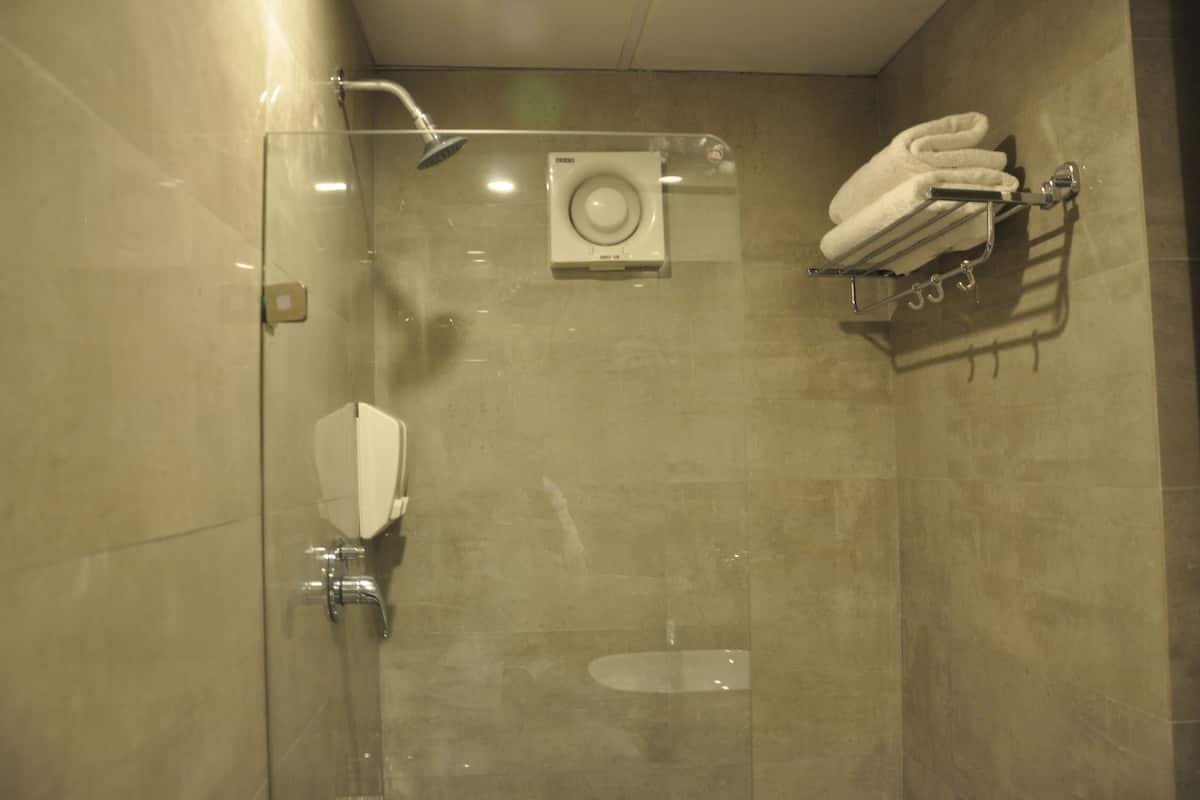 A glass-enclosed shower with a handheld showerhead, a wall-mounted toilet, and a towel rack with folded towels.