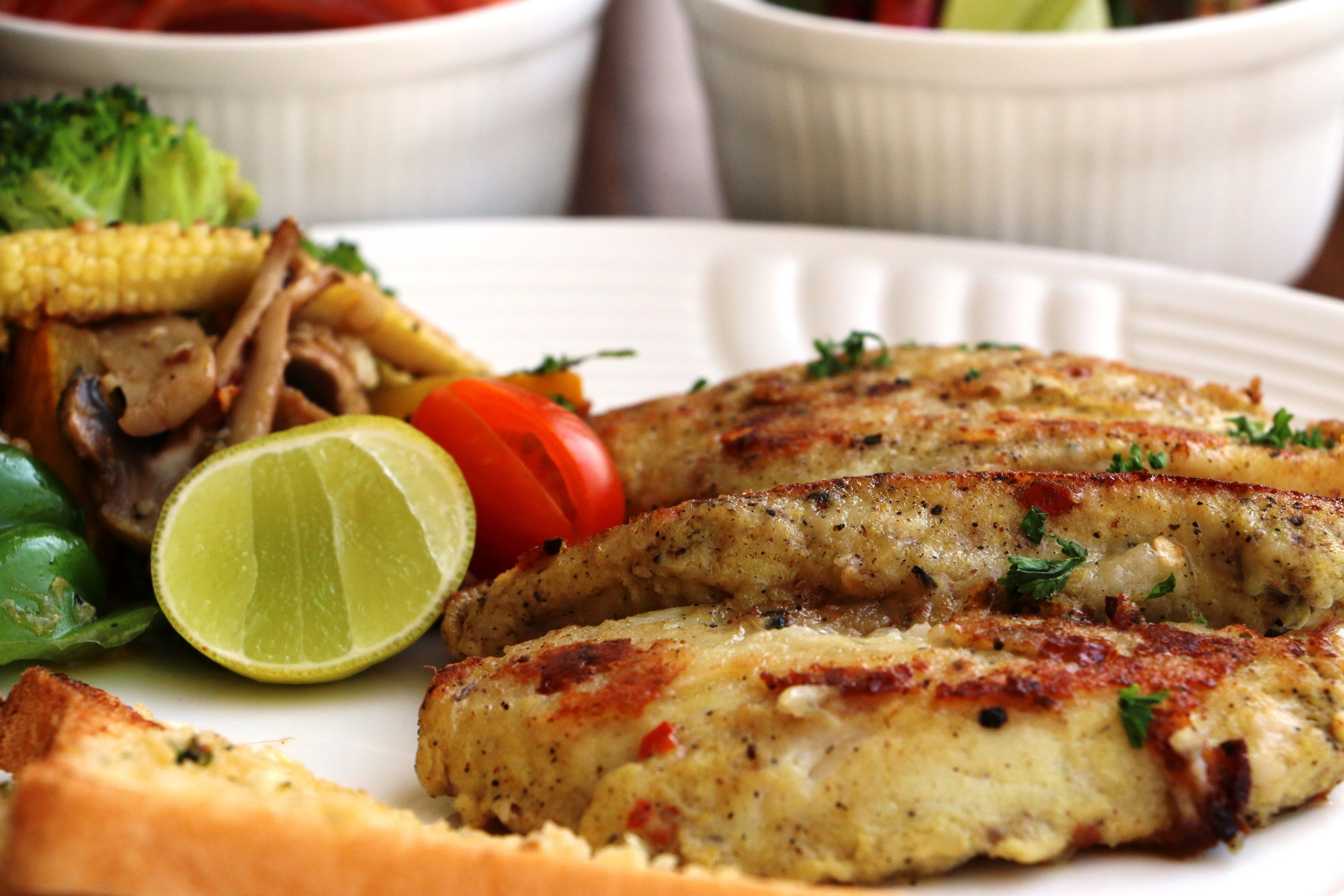 A plate of grilled chicken with vegetables and a slice of lime.