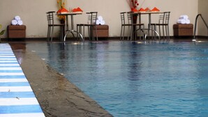 An indoor swimming pool with a blue and white striped edge, surrounded by tables and chairs with orange napkins. - Starlit Suites bangalore (Anekal)