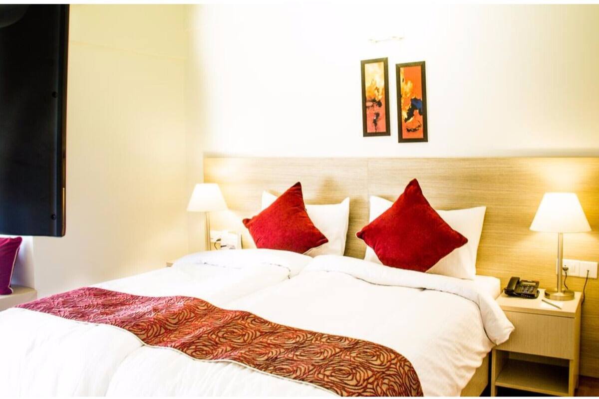 A hotel room with a bed, two bedside lamps, a nightstand with a phone, and two framed pictures on the wall.