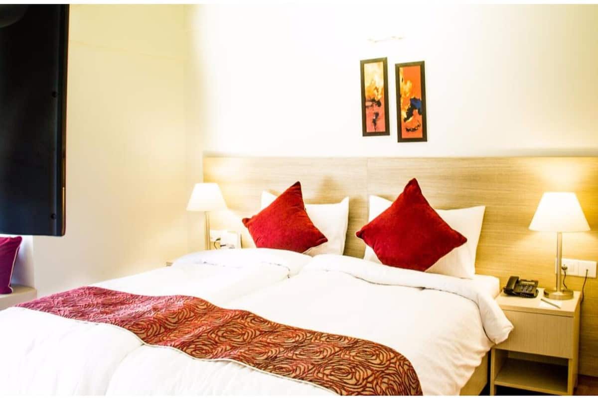Une chambre d’hôtel avec un lit, deux lampes de chevet, une table de chevet avec un téléphone et deux tableaux encadrés au mur.