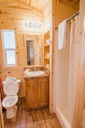 A wooden cabin bathroom with a toilet, sink, and shower.