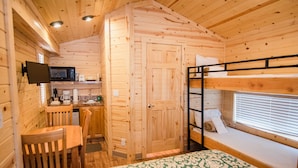 A wooden cabin interior with a bunk bed, a kitchenette, a dining area, and a television mounted on the wall.