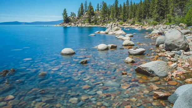 A clear lake with visible rocks and a forested shoreline.