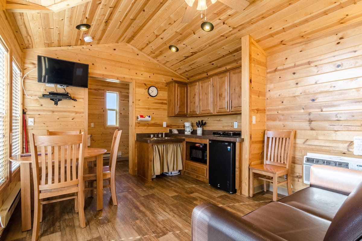 A wooden cabin interior with a dining area, kitchen, and seating space.