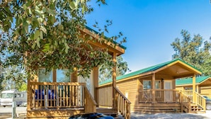 A wooden cabin with a porch, a barbecue grill, and a picnic table. - Wilderness Lakes RV Resort (Menifee)