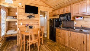 A compact wooden cabin with a kitchenette, a dining area, and a small bedroom. - Wilderness Lakes RV Resort (Menifee)