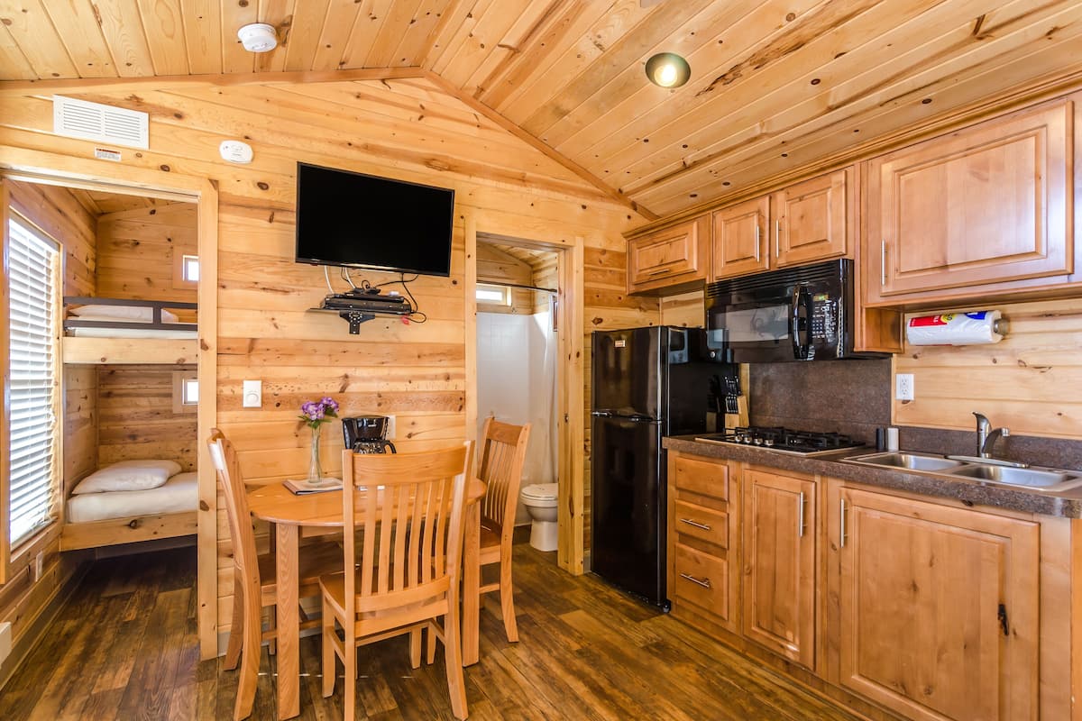 A compact wooden cabin with a kitchenette, a dining area, and a small bedroom.