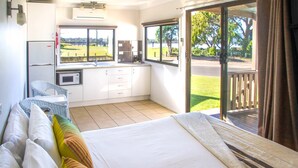 Un dormitorio con cama, un pequeño rincón de cocina y una puerta corrediza de vidrio que da a un espacio exterior.