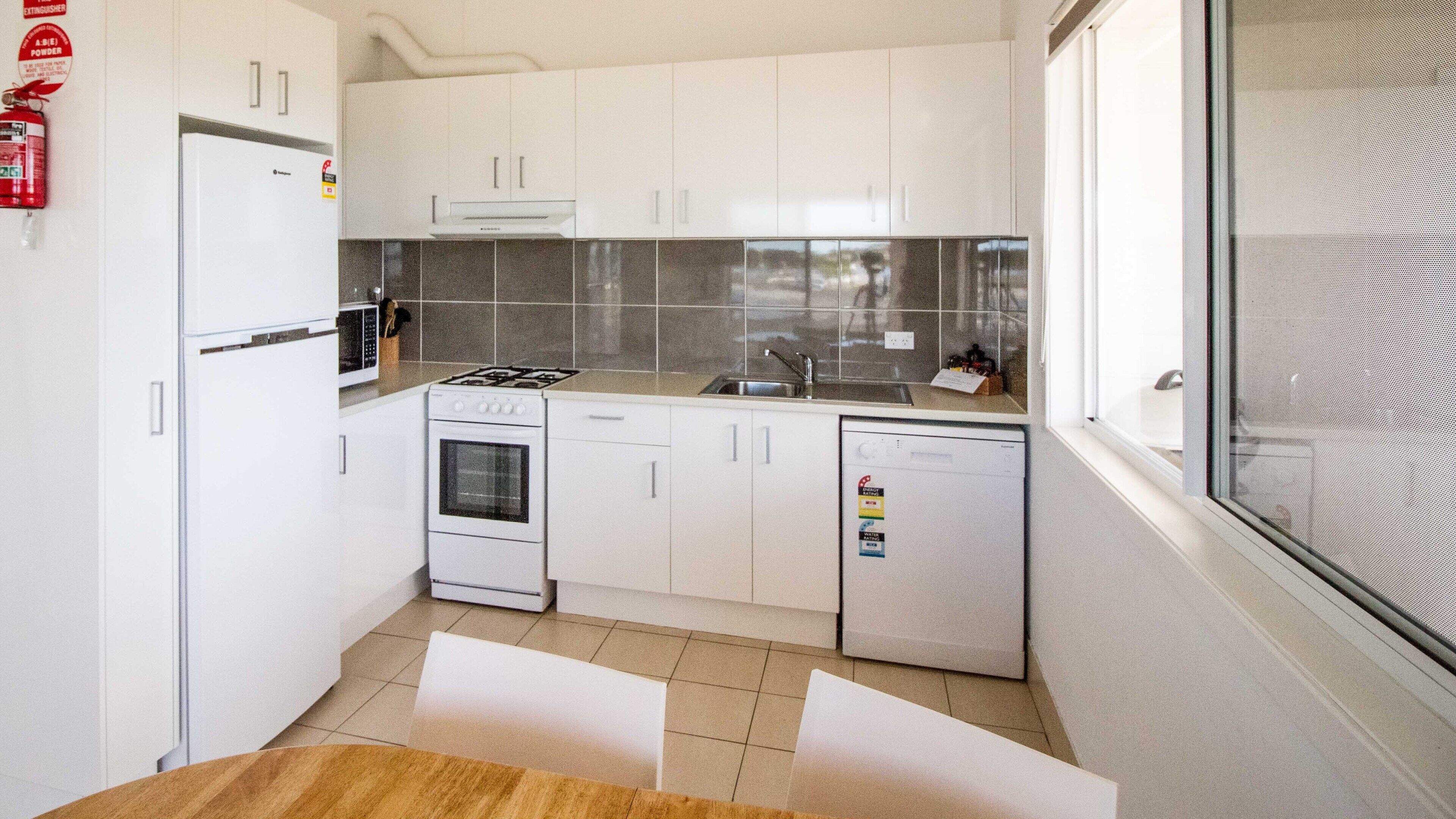 A compact kitchen with white cabinets, a stove, oven, microwave, and dishwasher.