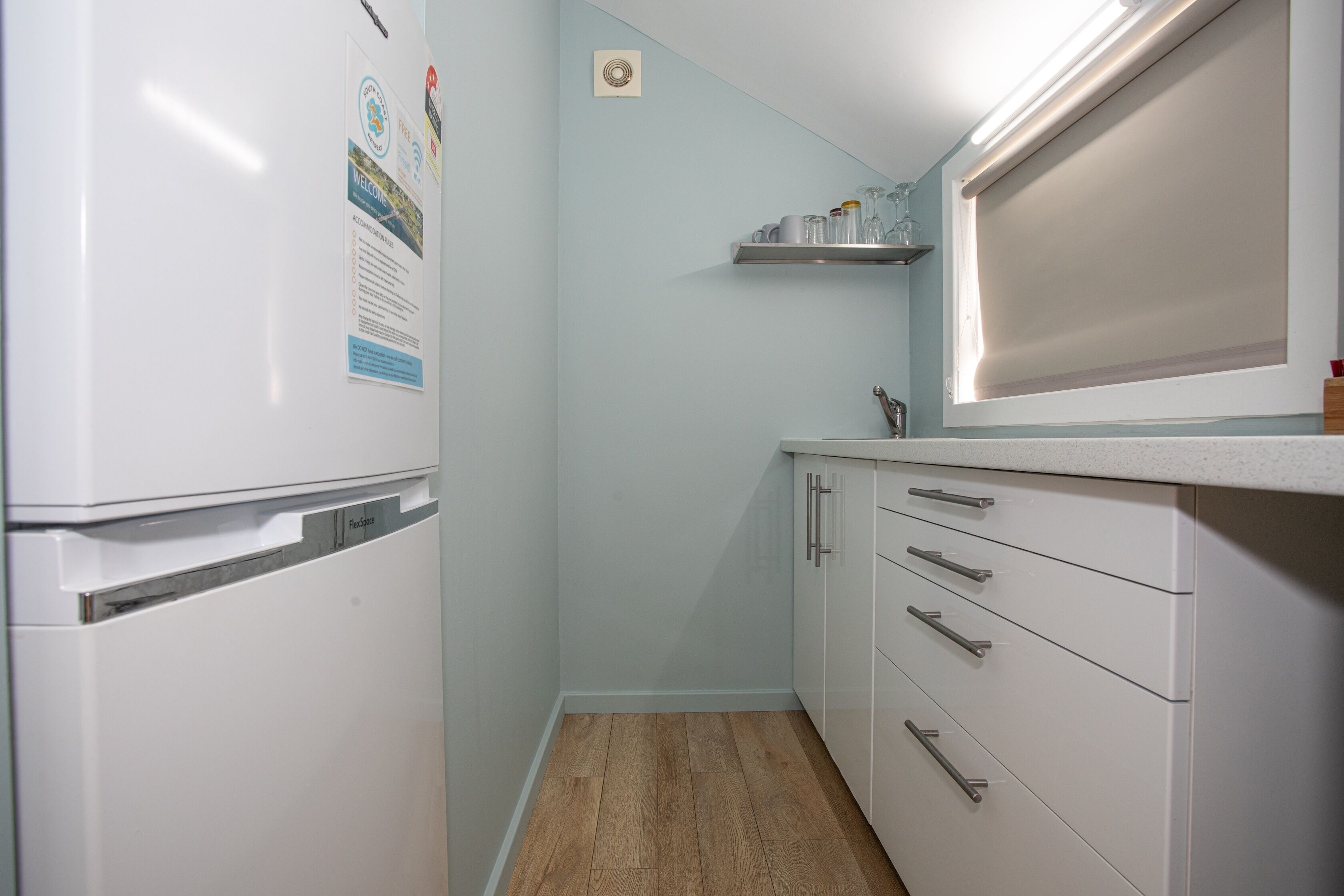 A compact kitchen with a white refrigerator, a wooden floor, and a white countertop with a sink.
