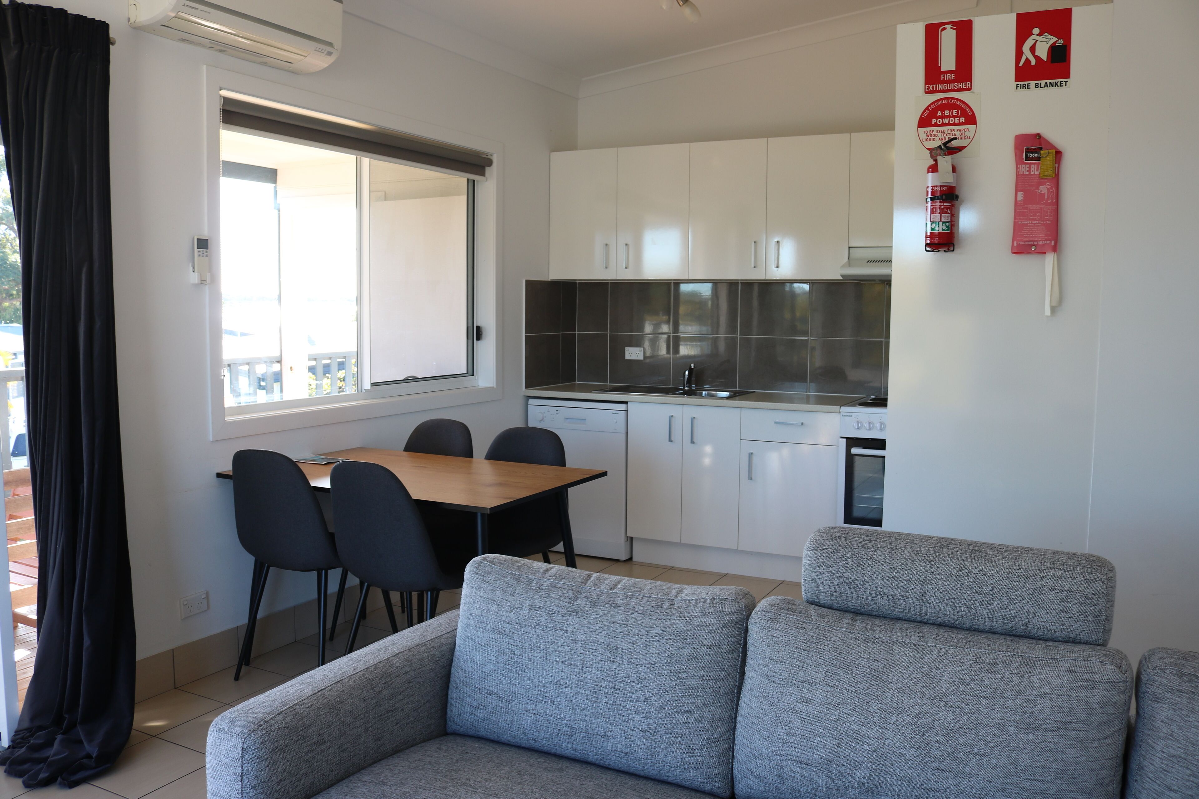 A modern kitchen with white cabinets, a dining table with chairs, and a grey sofa.
