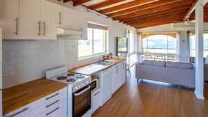 Una cocina moderna con armarios blancos, encimeras de madera y horno integrado. Hay un ventanal que proporciona luz natural y vistas al exterior.