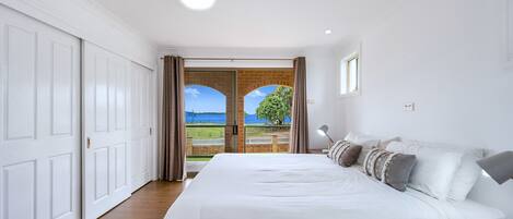 A bedroom with a large bed, a nightstand, a lamp, and a view of a green landscape through a glass door.
