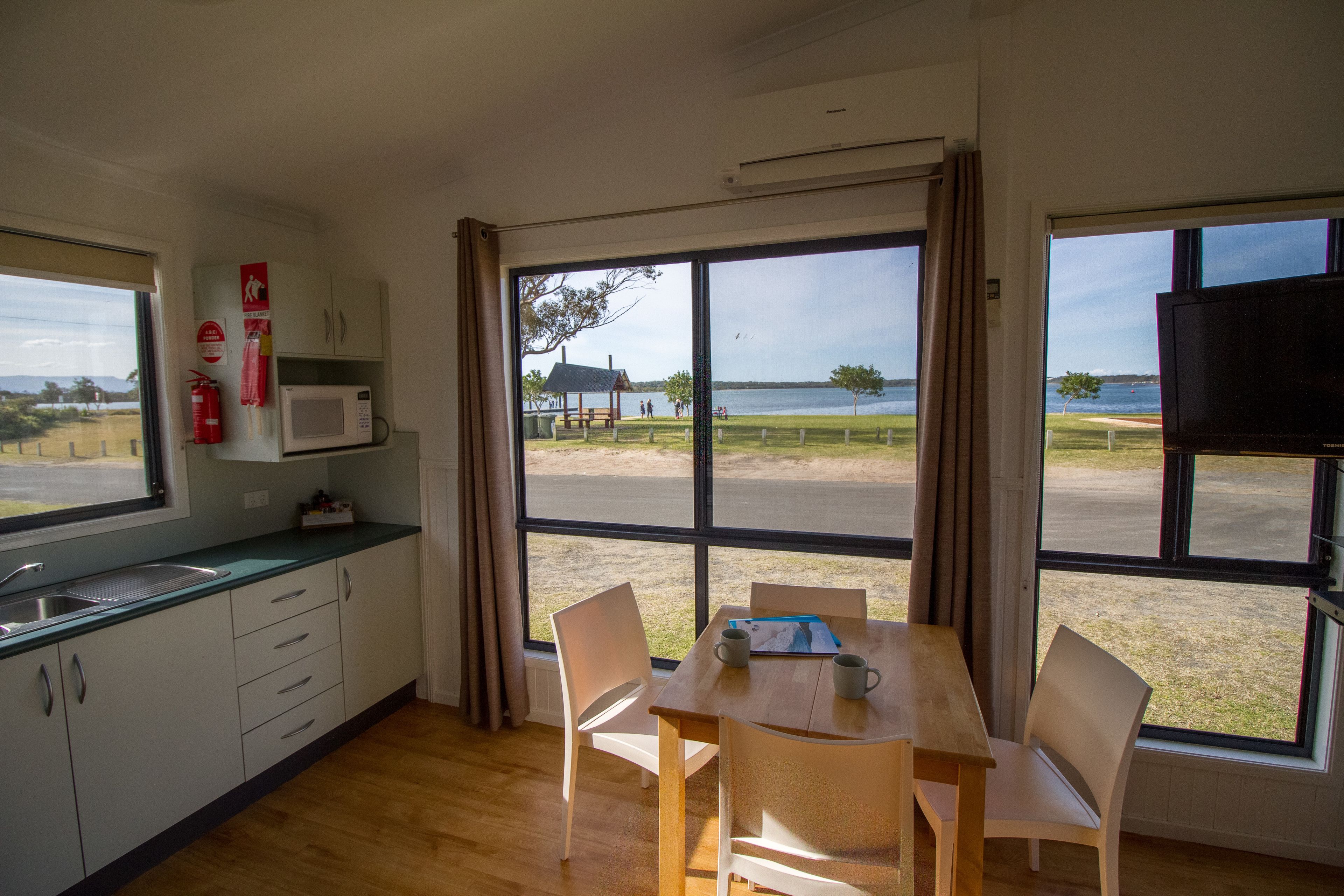 Una cocina con microondas, un lavamanos y ventana con vista a un área verde.