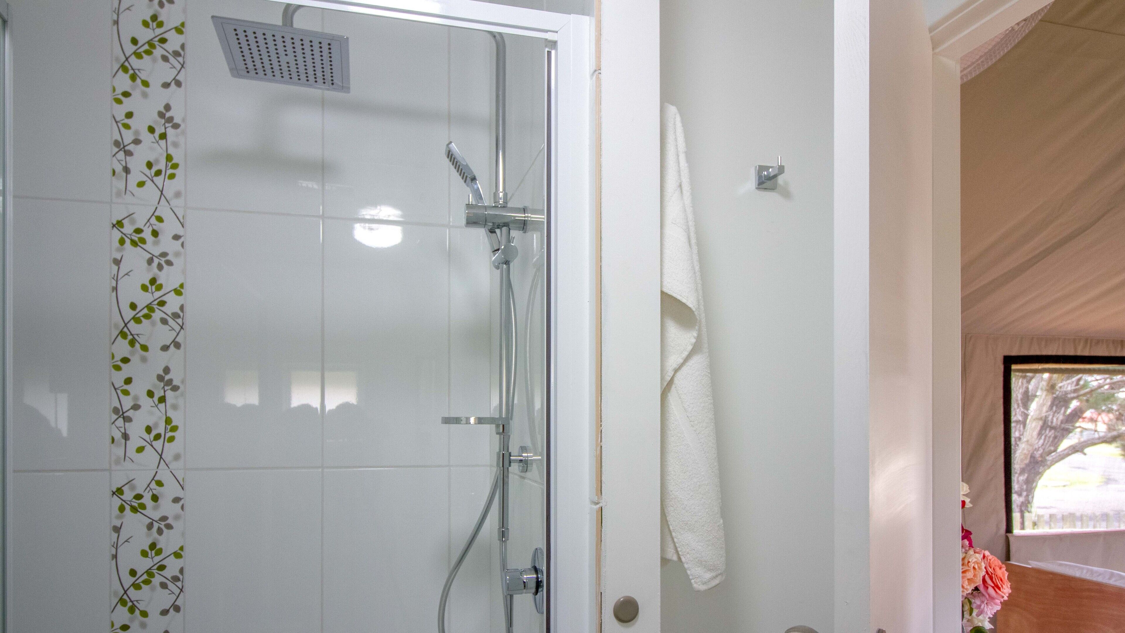 Ducha con puerta de vidrio, una toalla blanca colgada en la pared y una ventana con vistas a árboles.